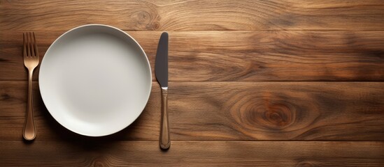 Poster - An eating concept is depicted in the image of a spoon and fork alongside a white dish placed on a wooden table with copy space