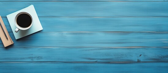 Fototapete - A top down view of a blue wooden table with a coffee cup and an empty notepad providing ample space for additional content in the image