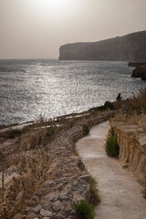 Wall Mural - a walkway leading to the beach at sunset by a rocky path: Xlendi Bay in Gozo island in Malta