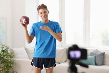 Poster - Smiling sports blogger holding american football ball while recording fitness lesson with camera at home