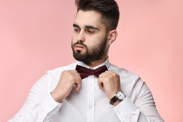 Wall Mural - Portrait of handsome man adjusting bow tie on pink background