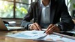 © Matthew - A professional in a suit reviews data charts and financial reports at a desk with a laptop and calculator
