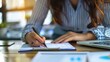© Matthew - Close-up image of an individual's hands as they write in a spiral notebook, with papers and laptop in the background