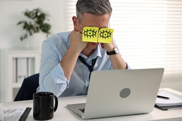 Wall Mural - Man with fake eyes painted on sticky notes snoozing at workplace in office