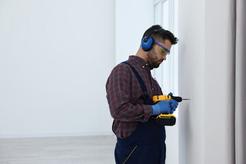 Canvas Print - Young worker in uniform using electric drill indoors, space for text