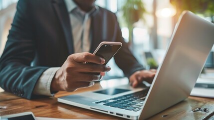 Businessman using a smartphone and laptop simultaneously at a desk