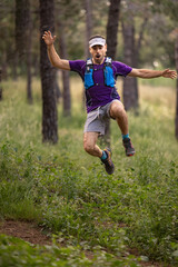 Wall Mural - A man in a purple shirt and blue shorts is jumping in the air. He is wearing a blue hat and a blue backpack