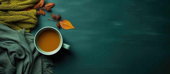 Poster - Knitted scarf with warm cup of tea on green background Autumn Fall season Still life Top view Falt lay Copy space