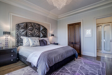 Wall Mural - Elegant art deco bedroom captured from the front showing a charcoal grey geometric headboard, a lavender area rug, and a crystal ceiling light.