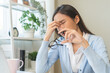 © KMPZZZ - Exhausted, asian young business woman working at office desk, took off eye glasses, massage rubbing nose from dry eyes, suffer on work hard, using laptop computer at office home, problem overtime job.
