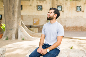 Happy young hispanic man wearing a gray t-shirt mockup, relaxing outside in a sunny urban setting