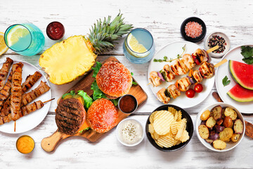 Wall Mural - Summer BBQ food table scene. Hamburgers, meat skewers, potatoes, fruit and snacks. Above view on a white wood background.