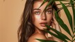 © Orod - Beautiful model with long, brown hair posing against a soft beige background with a green palm leaf, emphasizing natural beauty and glowing skin.