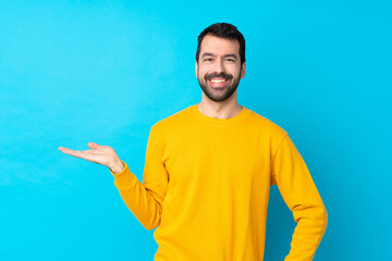 Wall Mural - Young caucasian man over isolated blue background holding copyspace imaginary on the palm to insert an ad