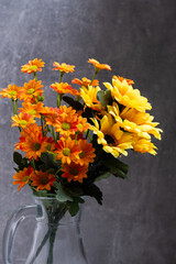 Bouquet yellow and orange flowers in jug on dark background.