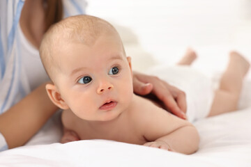 Wall Mural - Woman applying body cream onto baby`s skin on bed, closeup