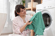 © New Africa - Happy young housewife with laundry near washing machine at home