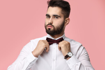 Wall Mural - Portrait of handsome man adjusting bow tie on pink background