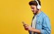 © Tui - Man in blue shirt, white headphones using smartphone on yellow background.
