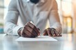 © stockpro - Close-up view of a person writing on paper at a desk in a bright office, emphasizing focus and professionalism.
