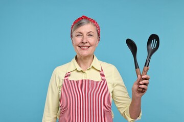 Canvas Print - Happy housewife with spoons on light blue background