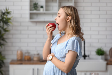 Canvas Print - Young pregnant woman eating apple in kitchen