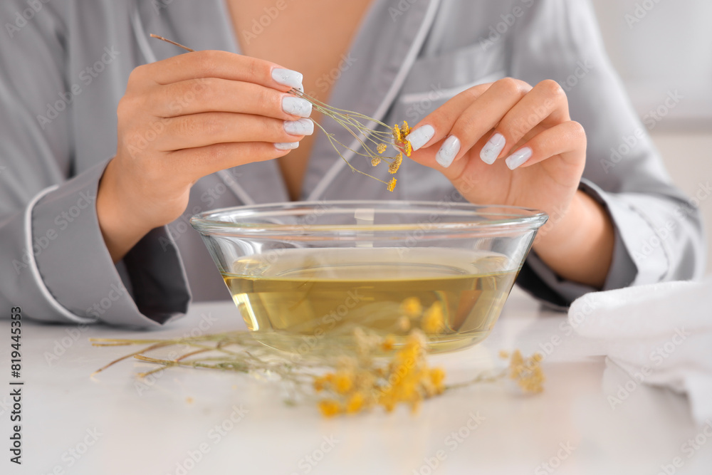 Young woman preparing steam inhalation with herbs at table in kitchen, closeup