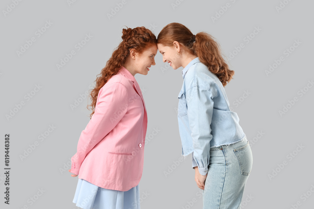 Stylish happy redhead sisters on grey background