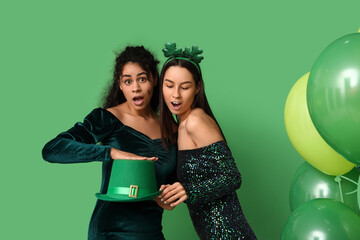 Poster - Shocked young women with leprechaun hat and air balloons on green background. St. Patrick's Day celebration