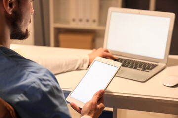 Sticker - Male nurse with tablet computer and laptop working evening shift at table in clinic, closeup