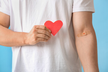 Wall Mural - Blood donor with applied medical patch and paper heart on blue background