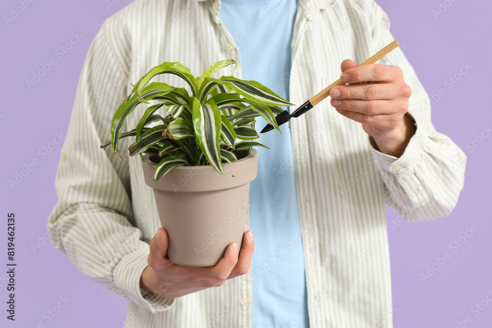 Young man with shovel and plant on lilac background, closeup