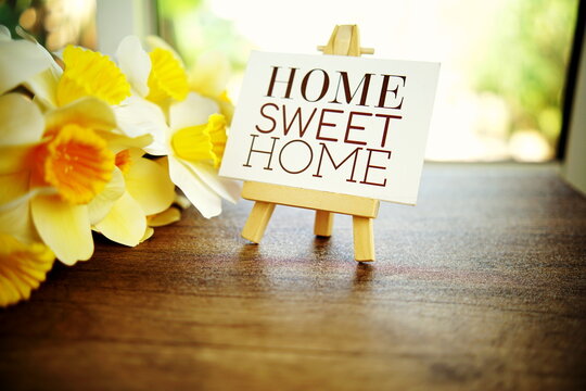 Home Sweet Home text message on paper card with wooden easel and flower decoration on wooden table background