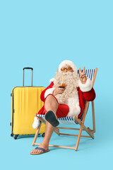 Wall Mural - Santa Claus with cocktail showing victory gesture in deck chair on blue background. Christmas in July