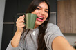 © Ladanifer - Happy female teenager with braces and a cup of tea taking a selfie in the kitchen.