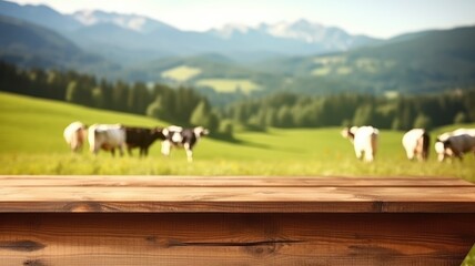 Wall Mural - Wooden table foreground with alpine meadow and cows with mountain backdrop. Rural life and eco-tourism concept. Cow walking and eating grass at animal farm with green mountain and blue sky. AIG35.