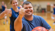 © Frank Gärtner - Young adult with down syndrome smiling and giving a thumbs up while holding a basketball in a lively gym environment