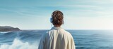 Fototapeta  - A man in a bathrobe and earphones with slouched shoulders gazes thoughtfully at the ocean waves with the horizon ahead creating a contemplative scene in the copy space image
