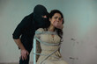 © Nataliya - Kidnapper in a black balaclava covering female mouth with his hand. Woman tied on a chair with a rope. Crime, kidnapping, violence concept