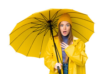 Sticker - Young pretty woman with rainproof coat and umbrella over isolated chroma key background surprised and shocked while looking right