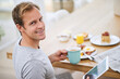 © peopleimages.com - Man, tablet and breakfast with smile in portrait for current events or information at dining table. House, food and weekend with meal for nutrition with entertainment or relaxing at home in Sweden.