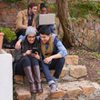 © peopleimages.com - College, laptop or students with phone on campus steps for learning, research or group project planning. Education, university or gen z friends with teamwork for classroom, assignment and support
