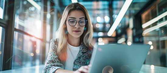 Poster - In a contemporary office setting, a businesswoman demonstrates productivity and professionalism while working remotely on a laptop, emphasizing connectivity and digital tools for efficient work