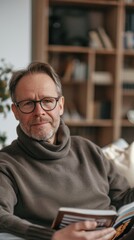 Poster - A man with glasses and a beard, wearing a brown sweater, sitting in a cozy room with a bookshelf in the background, reading a book.