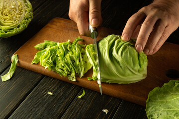 Sticker - Shredding cabbage with a knife in the hands of a man. The process of preparing sauerkraut on the kitchen table