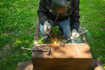 Wall Mural - A professional welder restores an old metal structure. Sparks from a welding machine in the hands of a welder outdoors