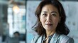 © iuricazac - A poised Asian woman with dark hair and a professional attire looking directly at the camera with a subtle smile set against a blurred background of an office environment.