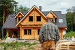 © Александр Марченко - A construction worker in a hard hat observing a log house under construction.