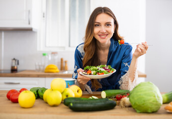 portrait of woman standing in home kitchen and tasting vegetable salad