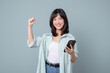 © Jirawatfoto - Excited asian woman, showing smartphone app and triumphing, celebrating on mobile phone, standing over green background